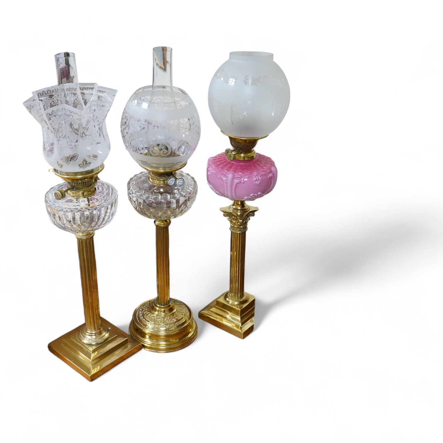 Three Victorian brass column oil lamps, with original brass fittings, glass reservoirs and shades. Tallest 72cm high.